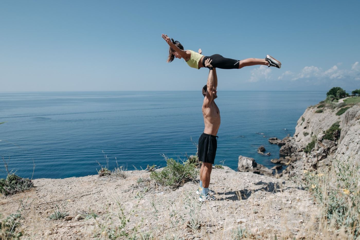 Two people practising acro yoga on rocks beside the sea