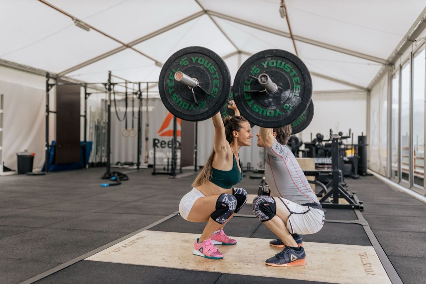 Two people doing barbell squats side by side in a gym
