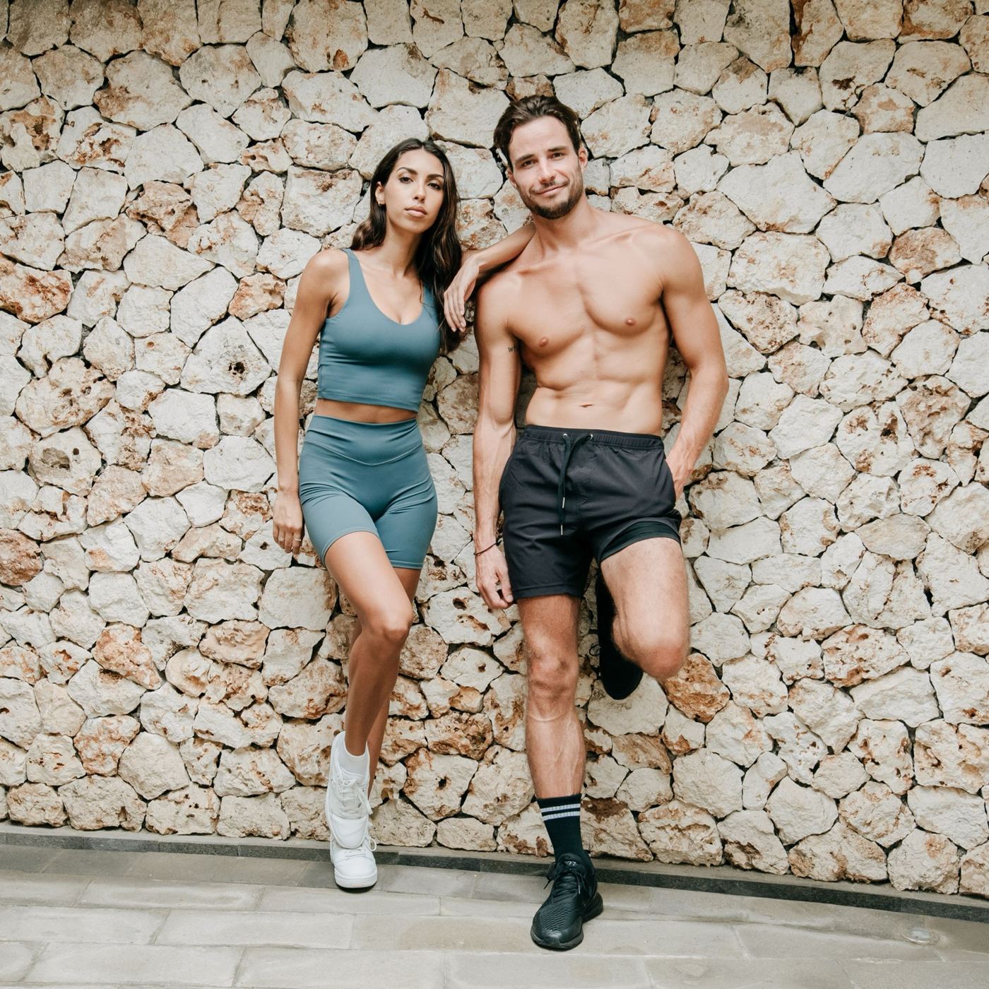 Active couple leaning against a stone wall in sportswear